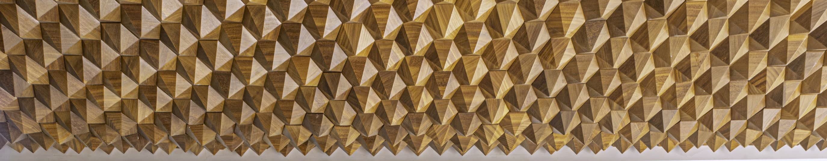 A full-width wall of hand-faceted walnut blocks catching raking light